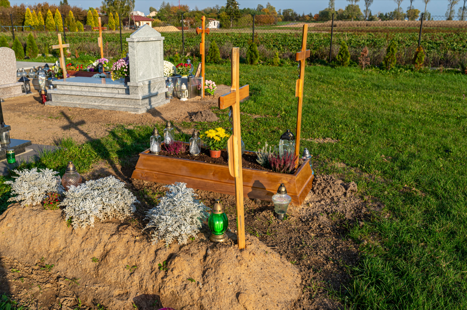 Frisch angelegte Gräber mit Holzkreuzen und Grablichtern auf einem Friedhof bei Sonnenschein