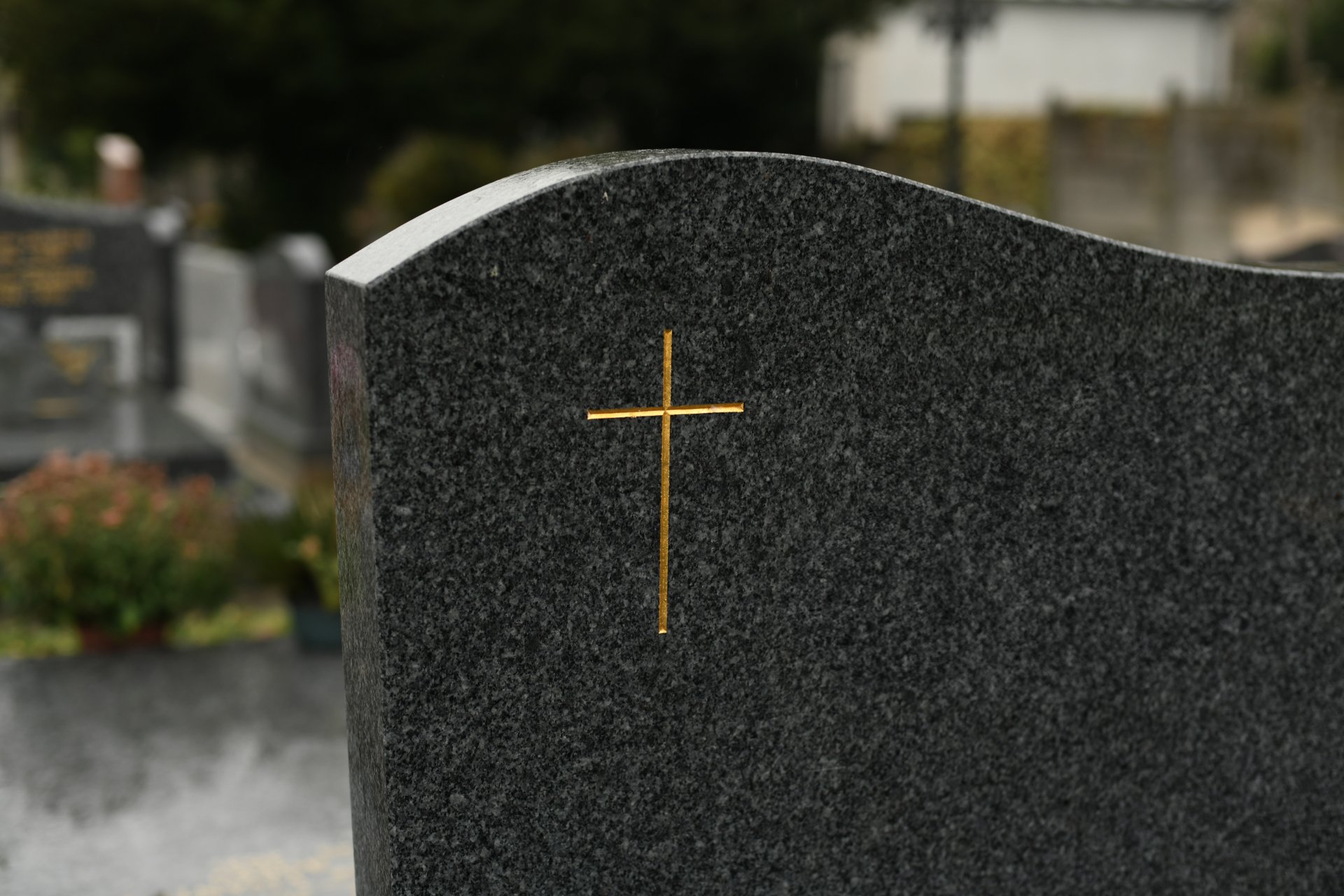 Grabstein aus dunklem Granit mit goldenem Kreuz auf einem Friedhof