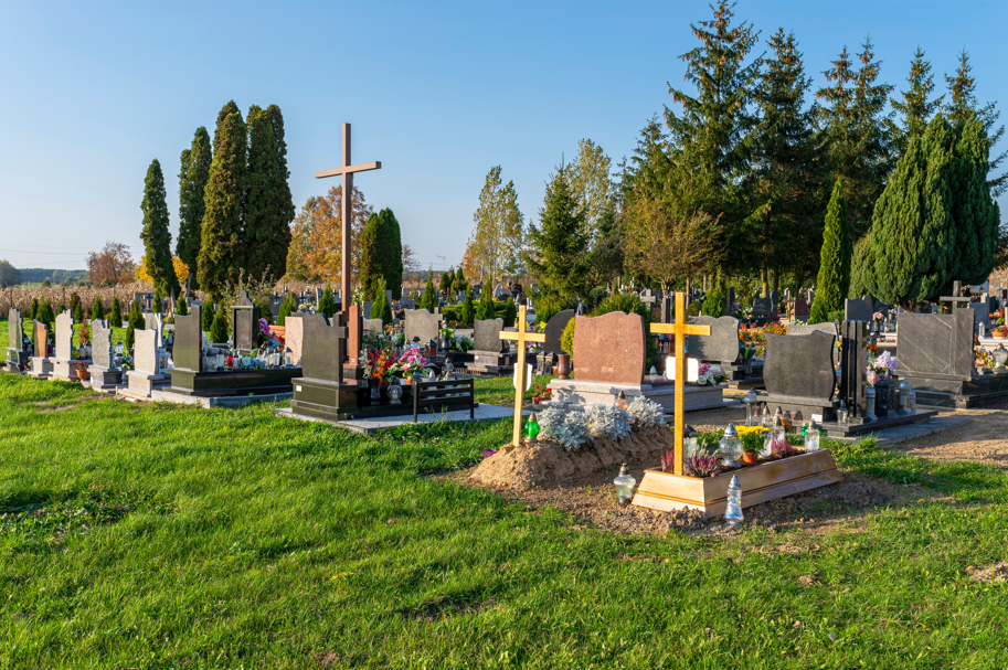 Friedhof mit verschiedenen Grabsteinen und Holzkreuzen, umgeben von Bäumen unter klarem Himmel